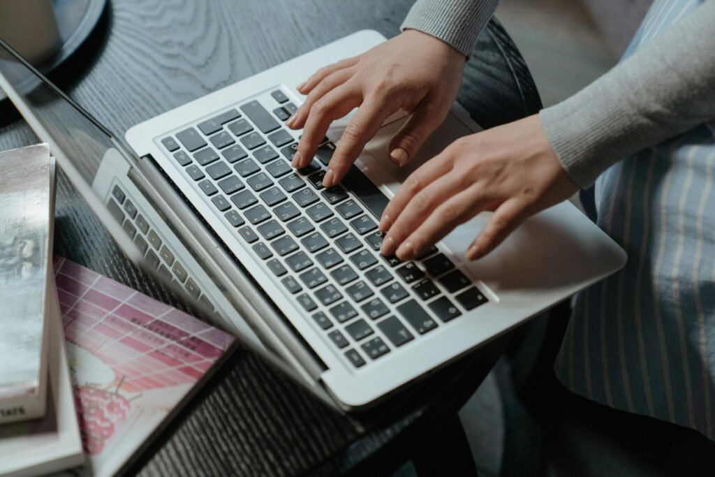 Close-up of a woman's hands typing on a laptop indoors, with books on the table.
